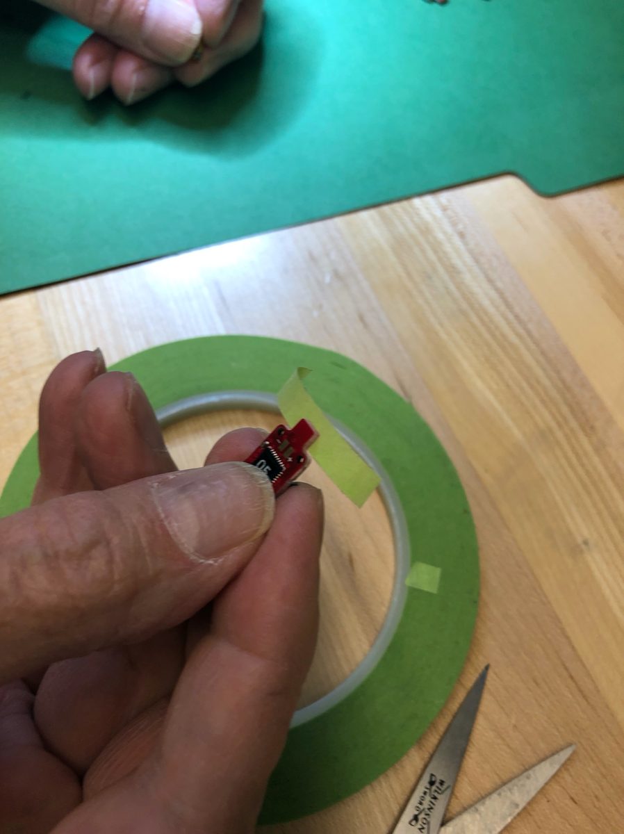 A tag board held in the fingers with masking tape being applied near the battery stem