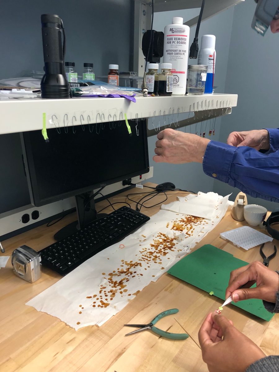 A work bench during coating, with tags hanging under a shelf and coating drips on paper towel
