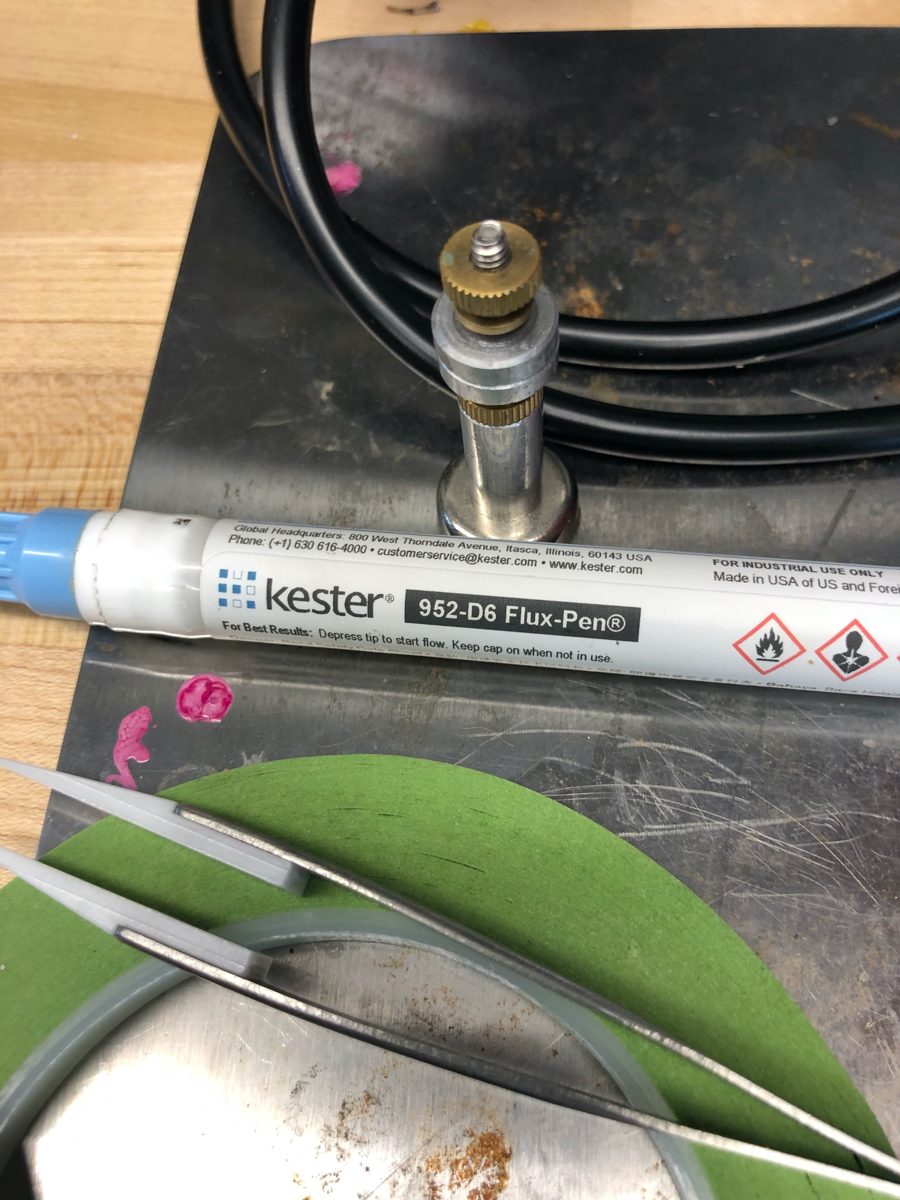 Kester 952-D6 flux pen lying on a steel work surface beside tweezers